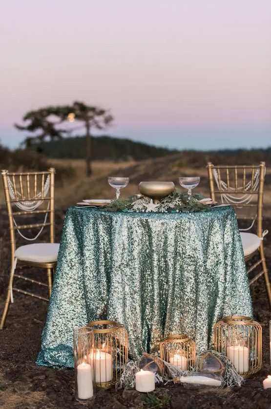 a mermaid table setting with an aqua sequin tablecloth and touches of brass for a chic look