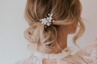 a messy and textured low ballerina bun with a volume on top and locks down, with a delicate floral hair pin