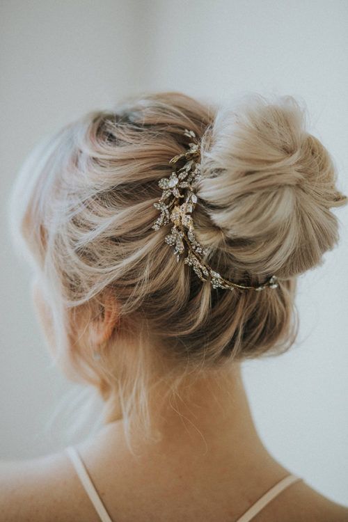 a messy and volumetric top knot with a lovely embellished hair piece and some locks framing the face is chic
