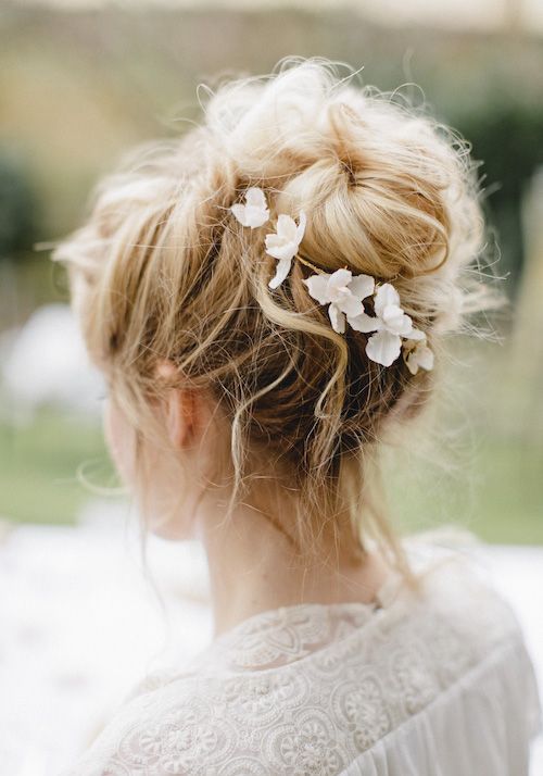 a messy and volumetric top knot with some locks down and white blooms is a catchy and chic idea to rock