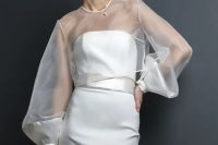 a minimalist bridal look wiht a strapless plain wedding dress with a sash and a sheer dress topper with long sleeves
