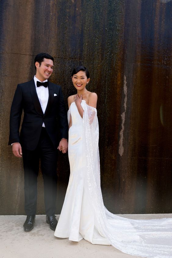 a modern plain strapless wedding dress with a pleated skirt and a train plus a shiny capelet for a modern or minimalist look