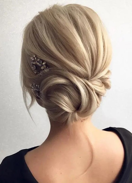 a side twisted low bun with some locks down and a rhinestone hairpiece on one side