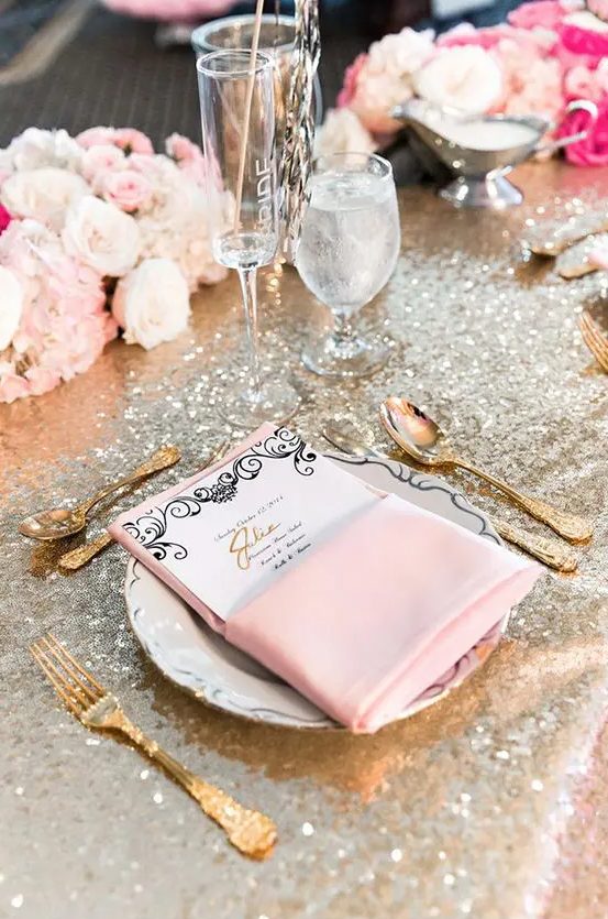 a silver tablecloth, pink napkins, a menu, blush and white blooms, gold cutlery and candles are lovely for a glam tablescape