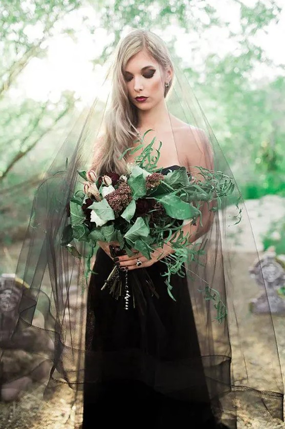 a strapless black lace wedding dress, a black smokey eye, a bold lip, a black veil and a moody bouquet for a gorgeous Halloween bridal look
