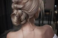 a voluminous braided updo with a large central braid and a low bun plus some locks
