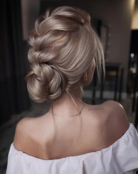a voluminous braided updo with a large central braid and a low bun plus some locks