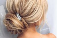 a voluminous updo with a wrapped low bun and a small feather hairpiece for an elegant touch