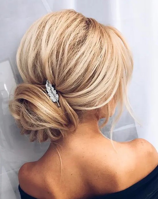 a voluminous updo with a wrapped low bun and a small feather hairpiece for an elegant touch
