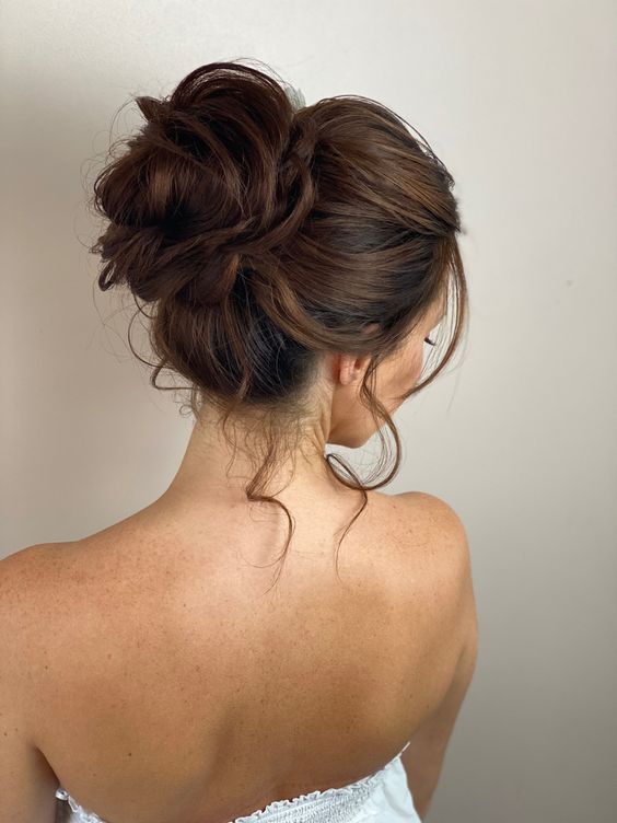 a wrapped and messy top knot with a bump on top and some locks down is a chic and catchy idea