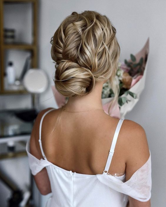 an eye-catchy wedding updo with a twisted low bun, a wavy top and some little waves on top to make it cooler