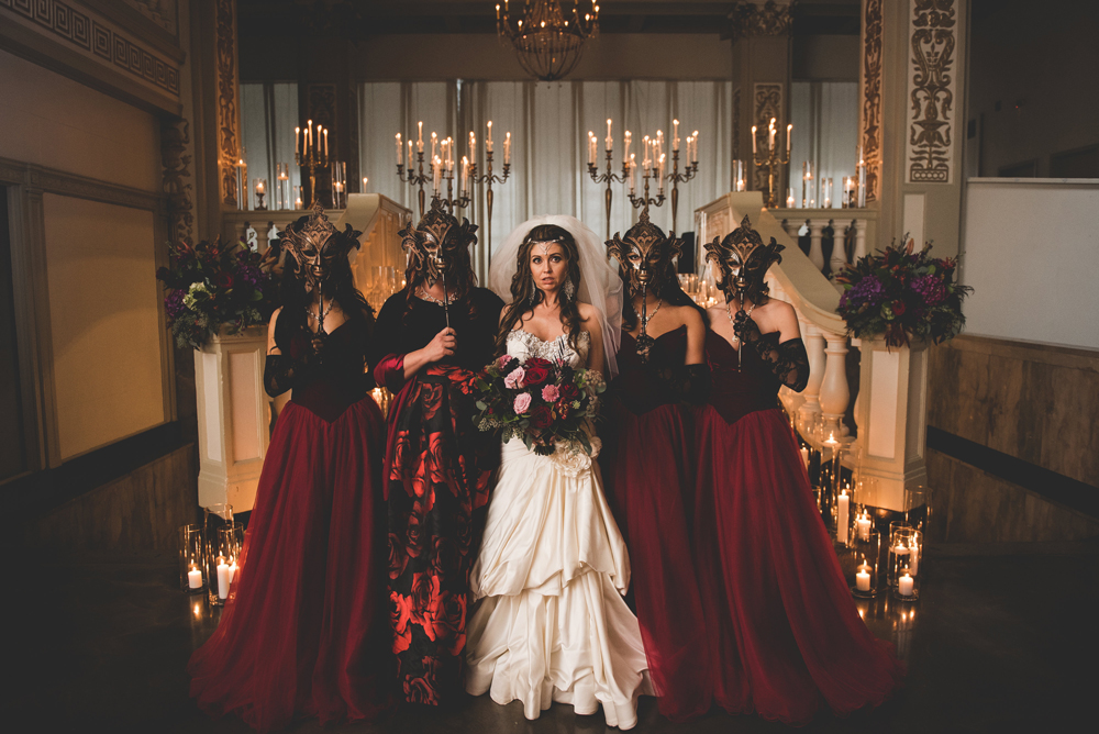 The bridesmaids were wearing burgundy ballgowns with velvet corsets and masks instead of bouquets