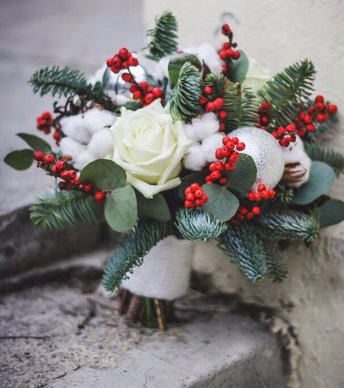 a Christmas wedding bouquet with holly berries, cotton, white roses and evergreens plus an ornament