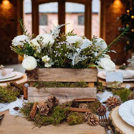 a rustic wedding centerpiece of a crate on moss, with pinecones and cinnamon bark, with white blooms and evergreens