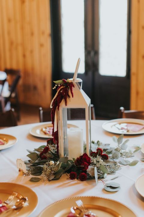 a winter wedding centerpiece of a white lantern with maroon blooms and greenery