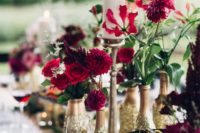 13 small vases made of gold and gold glitter bottles with bright red blooms and greenery for a festive tablescape