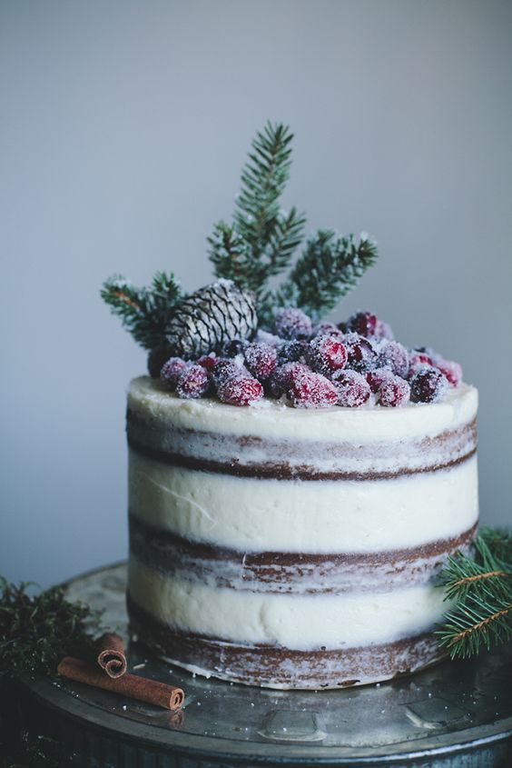 a semi naked wedding cake topped with a pinecone, evergreens and sugared berries for Christmas