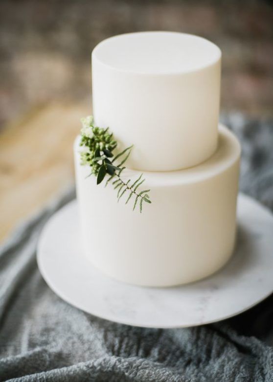 a pure white minimalist wedding cake decorated with some greenery for a Scandinavian spring or summer wedding
