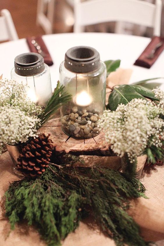 a rustic or woodland Christmas centerpiece of a wood slice, evergreens, pinecones,baby's breath, candle lanterns and pebble