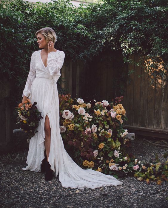 a boho lace wrap wedding dress with sleeves, a deep V-neckline, a slit and a ruffled skirt with a train, black boots