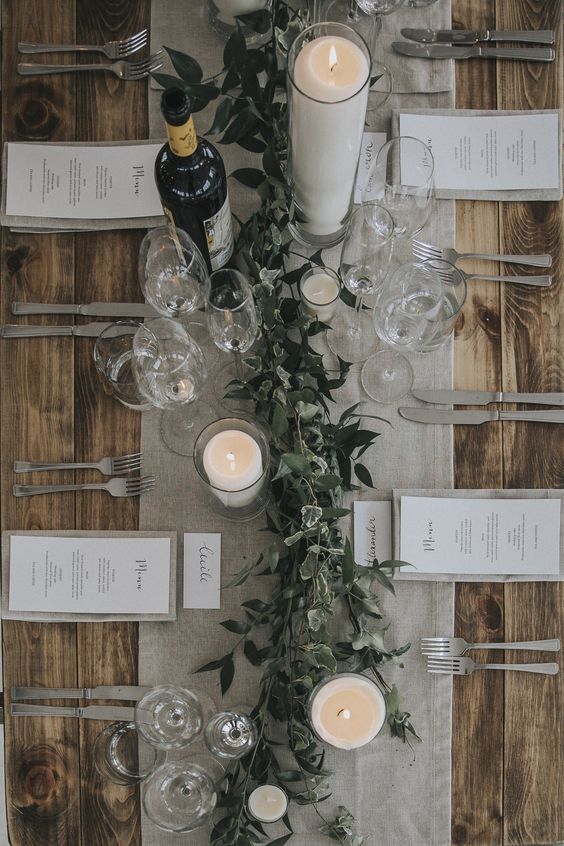 a grey table runner and napkins plus white candles and fresh greenery for a simple rustic look
