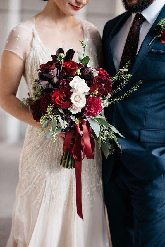 a luxurious wedding bouquet in the shads of red, deep purple and white with eucalyptus and red ribbons
