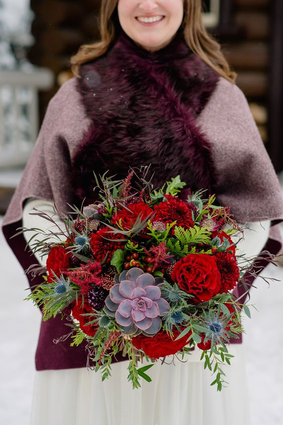a luxurious and bright wedding bouquet with red blooms, berries, thistles, colorful succulents and greenery