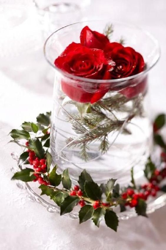 a Scandinavian wedding centerpiece with holly berries and a vase with evergreens and red roses floating in the vase