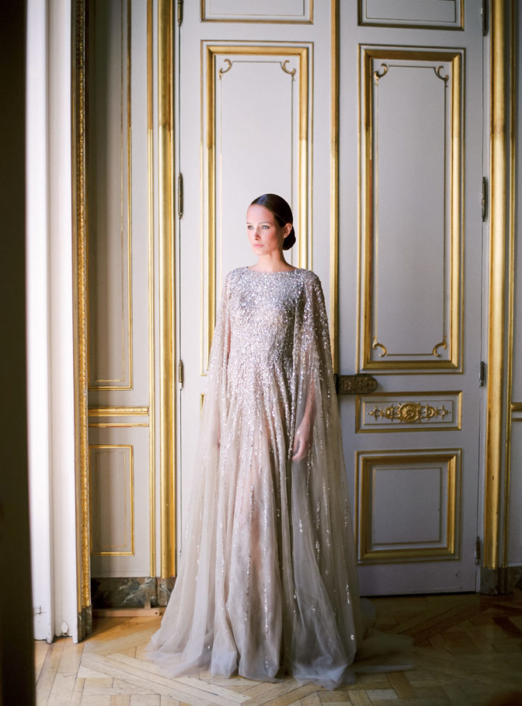 a silver grey wedding dress with heavy embellishments and a matching cape for a fashion-forward bride