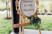 23 a vintage gold frame decorated with greenery and blooms and placed on an easel is a chic and sophisticated idea