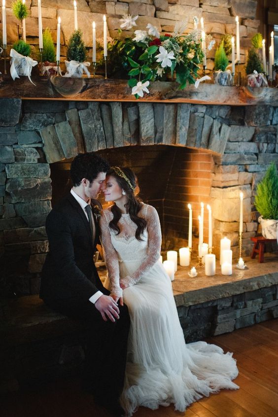 a cozy fireplace with candles and greenery and blooms and a couple by it