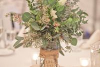 26 a textural rustic centerpiece of various foliage and some white blooms, the jar is wrapped with twine and a tag
