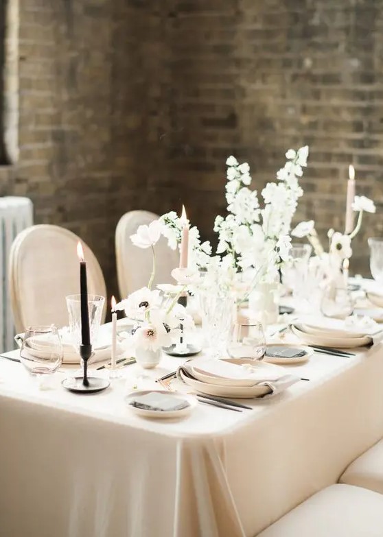 a beautiful and sophisticated neutral winter wedding tablescape with warm-colored linens and plates, white blooms, pink and black candles