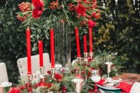 a bold Christmassy wedding tablescape with an evergreen and red rose table runner, a tall matching centerpiece, red roses and red napkins