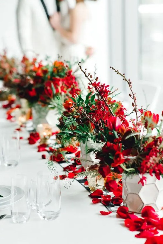 a bold red winter wedding table runner with bold red blooms, twigs and branches, greenery and petals on the world