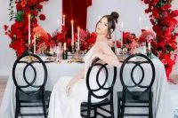 a bold rounded arch covered with red roses and matching red roses on the table for a refined and chic wedding tablescape