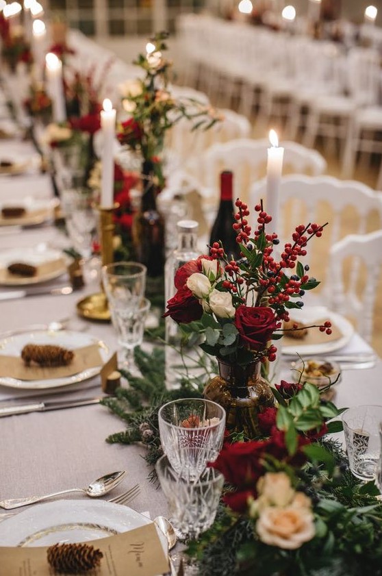 a bold winter wedding table with red and white blooms, berries, pinecones and evergreens looks lush