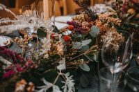 a bright floral table runner including fresh and dried leaves, berries and grasses is a cool and out of the box idea for a winter wedding