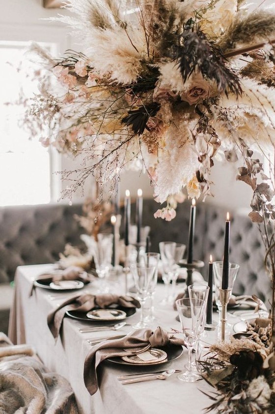 a chic winter wedding table with mauve napkins, black candles and all whites plus a large and chic dried bloom and herb overhead decoration
