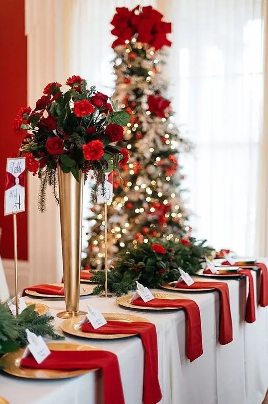 a classic Christmas wedding tablescape with greenery, fir and red and burgundy blooms and red napkins