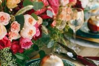 a colorful wedding tablescape with lush blush, pink and peachy blooms, greenery, green and gold plates and color block pomegranates