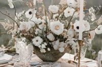 a frosty neutral winter wedding tablescape with a lush and large floral centerpiece, tall and thin candles and a pale pink table runner