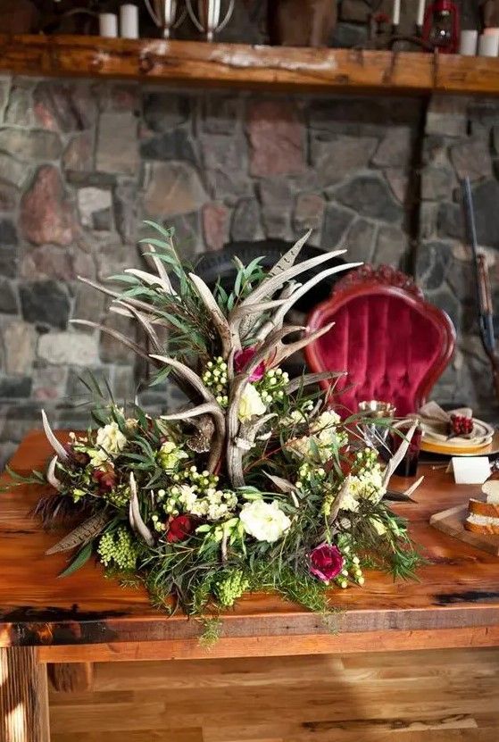 a gorgeous woodland-inspired centerpiece with antlers, different blooms, greenery and feathers