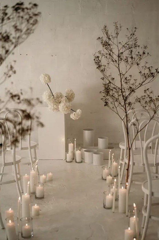 a jaw-dropping minimalist winter wedding space with white blooms, vases, dried branches and pillar candles