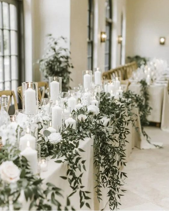 a luxurious winter wedding tablescape with white linens, white blooms, candles, greenery hanging down is a refined and beautiful idea to go for