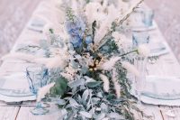 a neutral winter wedding centerpiece of blue blooms, dried herbs, greenery and berries is a cool idea for a frozen wedding
