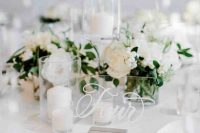 a pure white winter wedding centerpiece of blooms and berries, pillar candles and an acrylic table number