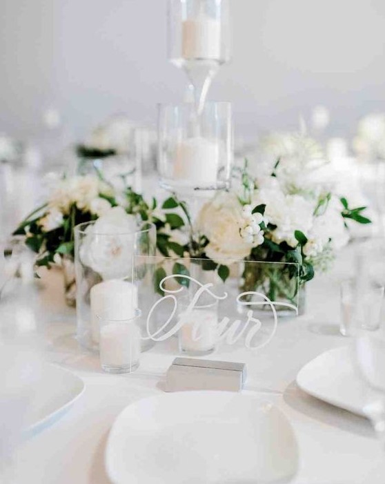 a pure white winter wedding centerpiece of blooms and berries, pillar candles and an acrylic table number
