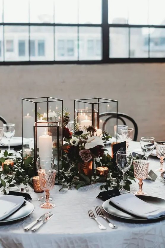 a refined winter wedding tablescape with white and dusty blooms, candles in candle lanterns, colored glasses and greenery