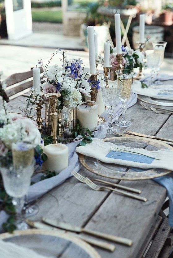 a rough winter wedding table with an uncovered table, pillar candles, white and purple blooms, twigs and refined glasses